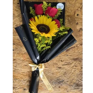 Ramo de mano con girasol y rosas rojas envuelto en papel negro con lazo dorado