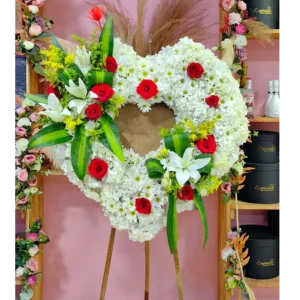 Corona floral de condolencias en forma de corazón con flores blancas y rosas rojas